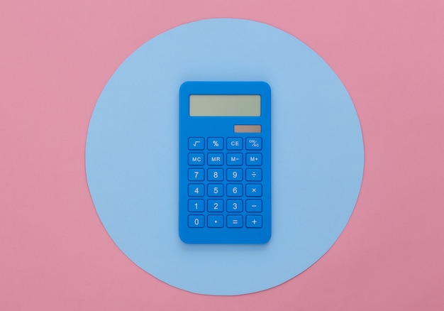 Calculatrice sur fond rose avec un cercle bleu. Prise de vue en studio conceptuel. Minimalisme. Vue de dessus