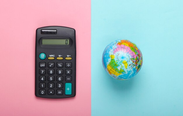 Calculatrice et globe sur fond pastel bleu rose. Vue de dessus