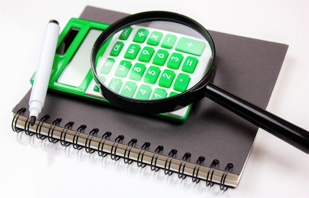 Calculatrice avec un marqueur avec un bloc-notes et une loupe sur un fond blanc isoléArticles d'affaires comptables