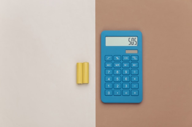 Calculatrice et piles sur fond beige marron. Vue de dessus