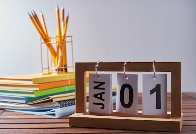 Calendrier 1er janvier avec pile de livre et porte-crayon contre le mur blanc