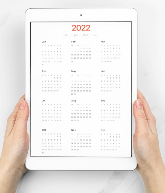 Calendrier 2022 à l'écran, mains avec tablette. Fond de marbre blanc. Photo conceptuelle de la planification du rendez-vous et de la réunion