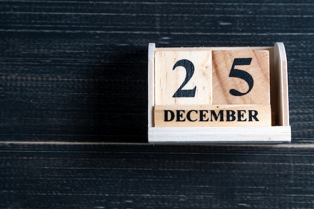 Calendrier de bloc en bois sur la date de Noël 25 décembre sur un fond en bois noir.