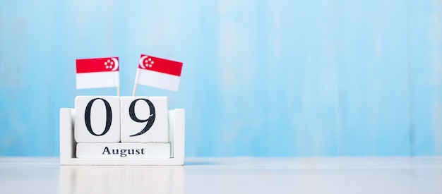 Calendrier en bois du 9 août avec des drapeaux de Singapour miniatures. Le jour de l'indépendance de Singapour, la fête nationale de la ville-état et les concepts de la république heureuse célébration