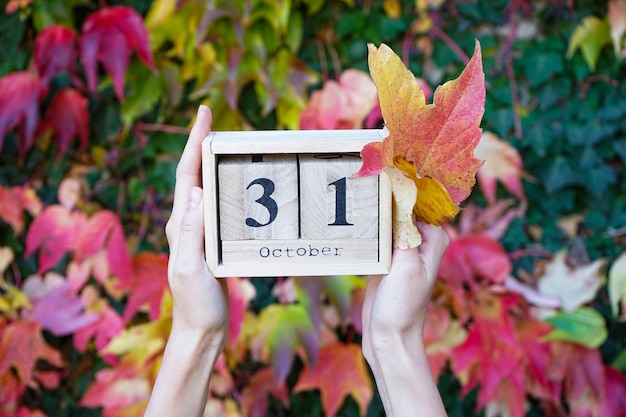 Photo calendrier en bois entre les mains d'une jeune femme la date est le 31 octobre sur fond de feuilles d'automne