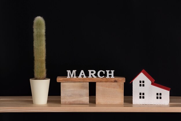 Photo calendrier en bois de mars, cactus et modèle de maison sur fond noir. espace de copie.