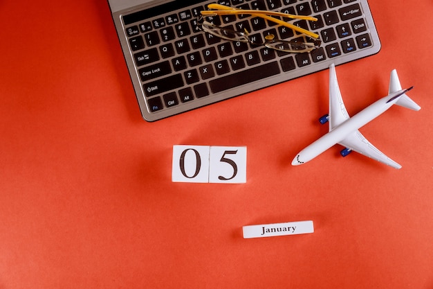 Calendrier du 05 janvier avec des accessoires sur le bureau de bureau de l'espace de travail sur le clavier de l'ordinateur, avion, fond rouge de lunettes