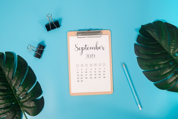 Calendrier plat avec presse-papiers, feuilles de palmier et crayon sur fond bleu