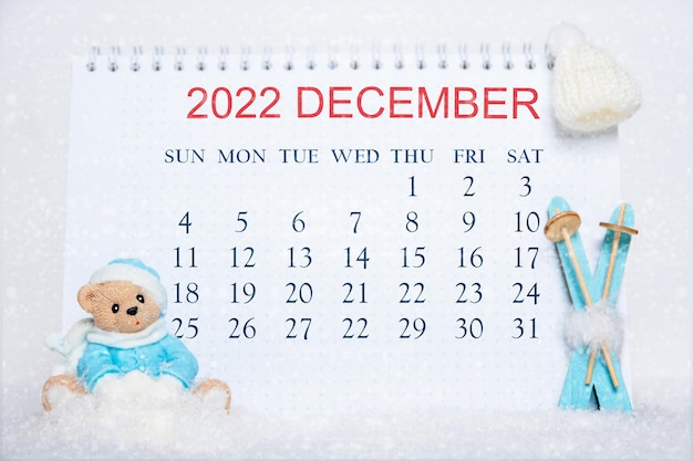 Calendrier pour le mois de décembre 2022 Carnet avec dates du calendrier et un jouet Ours en peluche en vêtements bleus skis bleus chapeau blanc sur neige blanche Calendrier pour le mois d'hiver Bonjour décembre