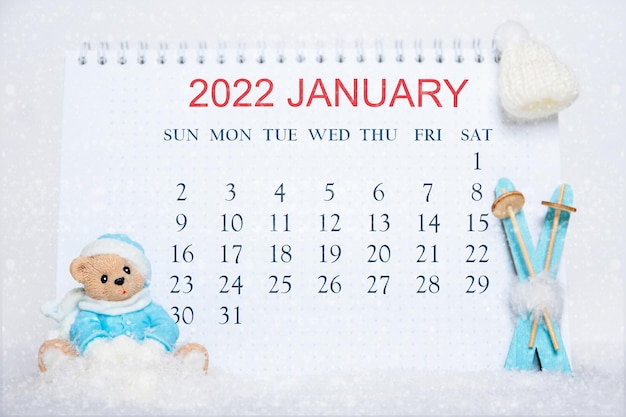 Calendrier pour le mois de janvier 2022. Bloc-notes avec les dates du calendrier et un ours en peluche en vêtements bleus, skis bleus, chapeau blanc sur neige blanche. Calendrier pour le mois d'hiver. bonjour janvier