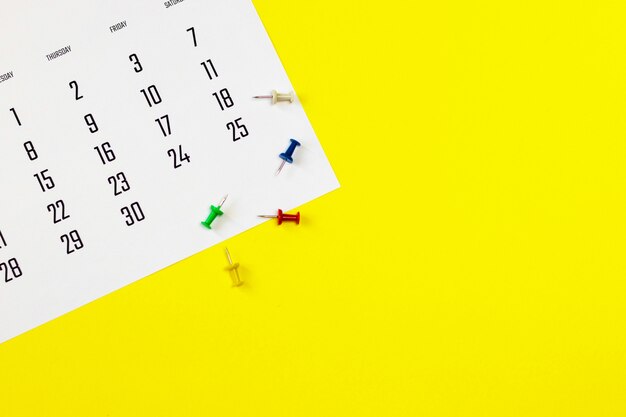 Calendrier et punaises sur fond jaune