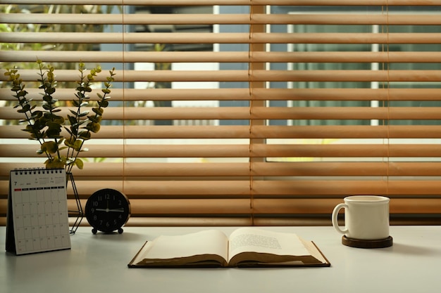 Un calendrier tasse à café livres réveil et plante en pot sur table blanche Bureau à domicile