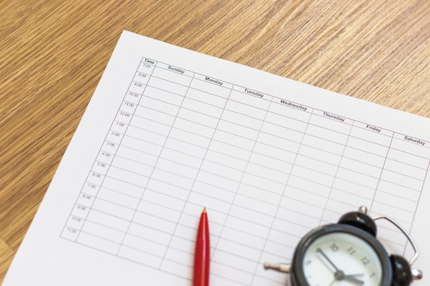 Calendrier vierge, calendrier hebdomadaire pour la planification des tâches. Mini réveil et stylo, flou. Vue de dessus, mise à plat.