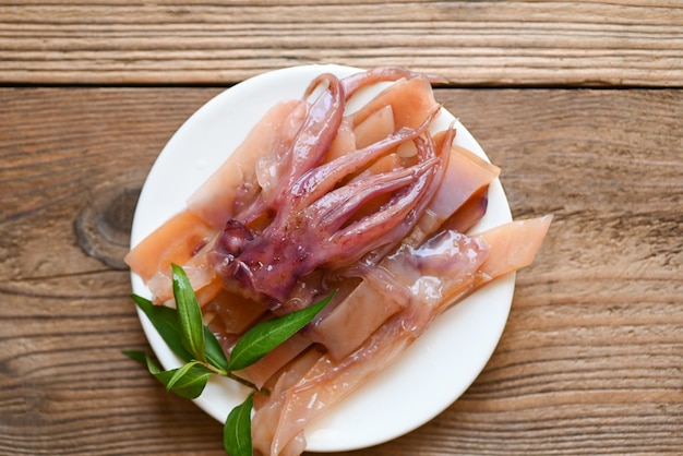 Calmars crus pour la cuisson des aliments sur une table en bois préservant les aliments calmars marinés de fruits de mer sur la vue de dessus de la plaque blanche