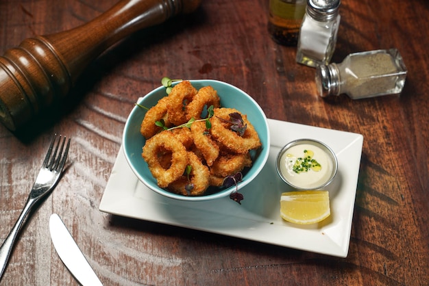 Calmars frits croustillants avec trempette et tranche de citron servis dans un plat isolé sur une table en bois vue de dessus de restauration rapide italienne