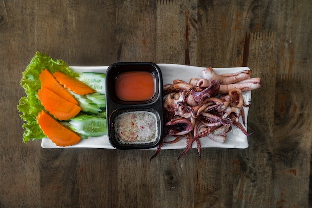 Photo calmars grillés sur un plat blanc avec sauce chili sur fond de table en bois