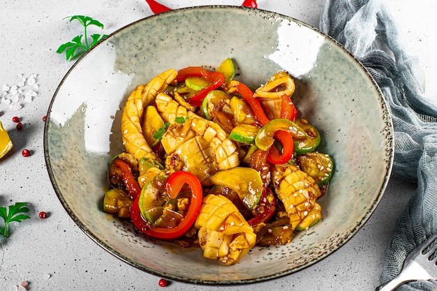 Photo calmars plats asiatiques traditionnels avec des légumes à la sauce aigre-douce sur une table en gros plan.