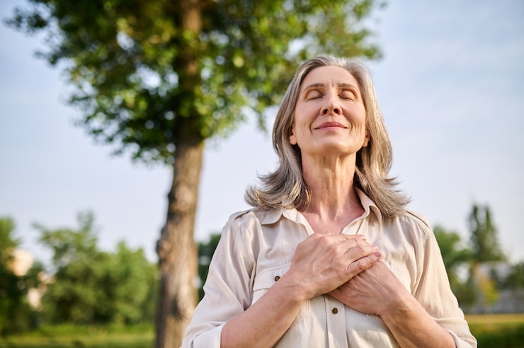 Photo calme. heureuse femme souriante adulte aux yeux fermés les mains jointes sur sa poitrine dans le parc d'été