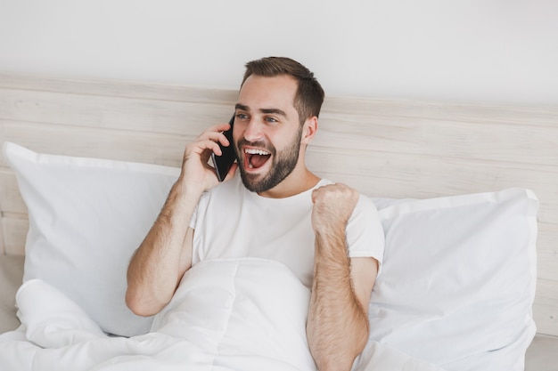 Calme jeune bel homme barbu allongé dans son lit avec une couverture d'oreiller en drap blanc dans la chambre à la maison