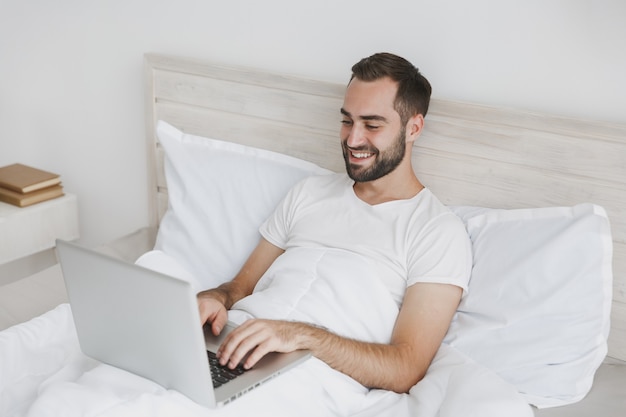 Calme jeune bel homme barbu allongé dans son lit avec une couverture d'oreiller en drap blanc dans la chambre à la maison