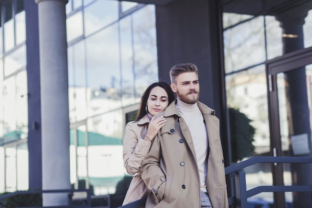 Calme jeune couple debout bras dessus bras dessous en manteau à l'extérieur