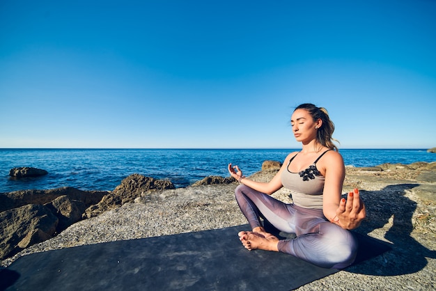 Calme jeune femme méditant sur la plage contre une belle mer bleue.