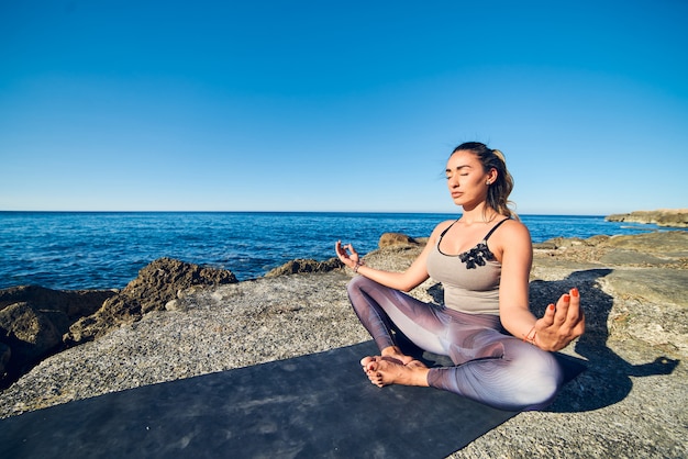 Calme jeune femme méditant sur la plage contre une belle mer bleue.