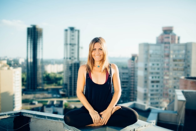 Calme jeune fille souriante assise sur un parapet en position du lotus