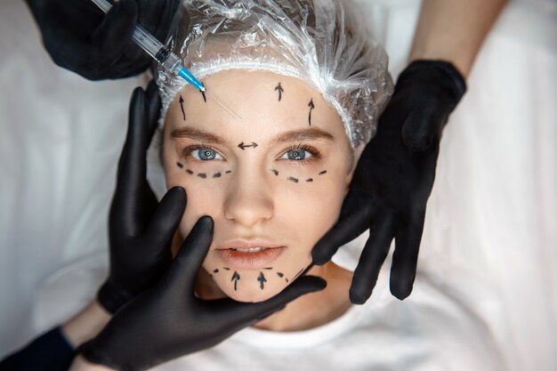 Calme paisible jeune femme allongée sur le canapé et regardez droit devant. Son visage est marqué. Trois mains touchant la peau du visage. Quatrième seringue de maintien pour injection.