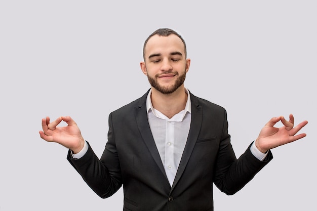 Calme et paisible jeune homme en costume méditant. Il garde les yeux fermés. Ses mains sont écartées du corps.