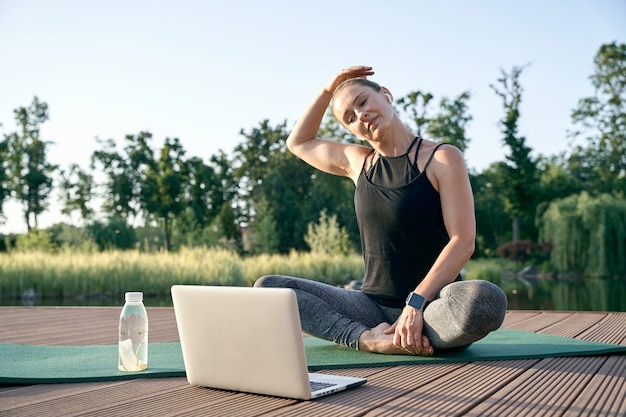 Calmez votre esprit athlétique belle femme d'âge moyen en regardant des vidéos pédagogiques sur un ordinateur portable tout en