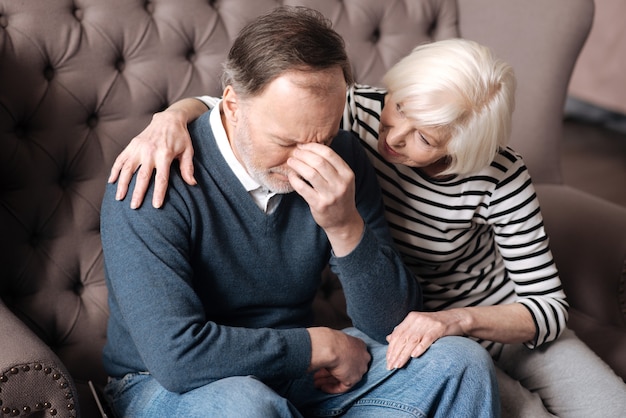 Calmez vous s'il vous plait. Une femme âgée est assise et embrasse son mari en dépression à la maison.