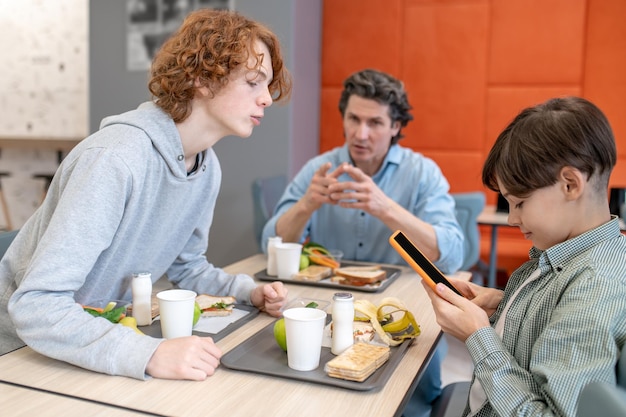 Des camarades de classe et leur professeur masculin assis ensemble à la table à manger de la cantine scolaire