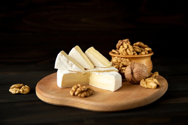 Camembert au fromage ou brie aux cerneaux de noix sur une planche à découper sur fond de bois noir. Espace de copie. Photographie d'atelier.