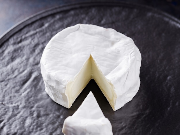 Camembert sur fond sombre. Fromage à pâte molle avec de la moisissure blanche sur une plaque noire. Minimalisme. Espace de copie