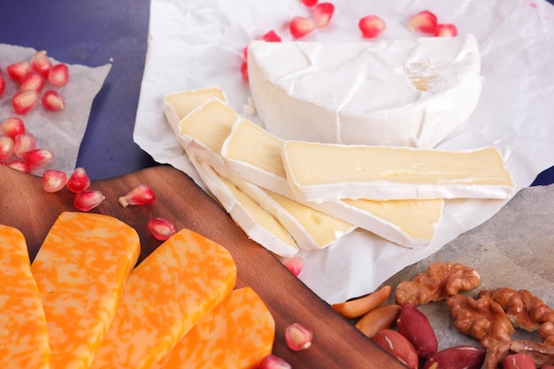 Photo camembert et fromage jaune à pâte dure avec grenade et noix sur fond bleu fromage sur planches de bois gros plan