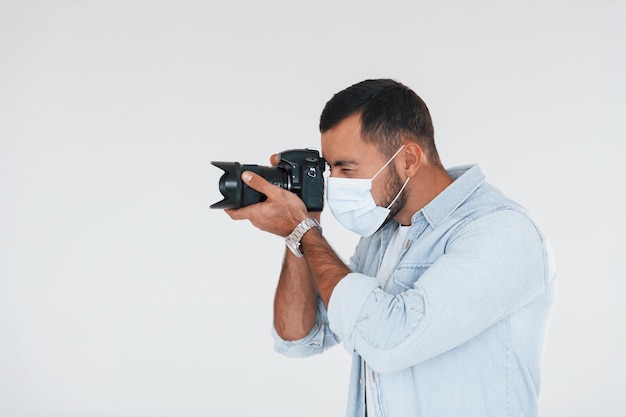 Avec caméra professionnelle jeune bel homme debout à l'intérieur sur fond blanc