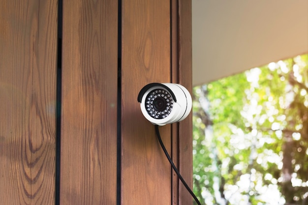 caméra de sécurité blanche sur le mur d'une maison en bois sur fond de paysage verdoyant