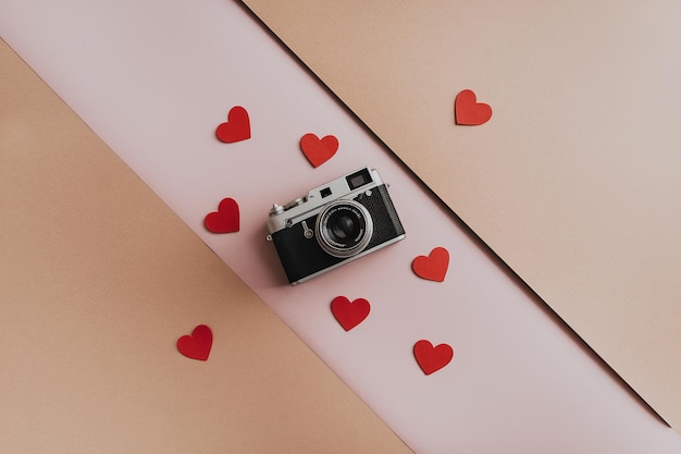 Une caméra vintage entourée de cœurs rouges sur un fond rose doux