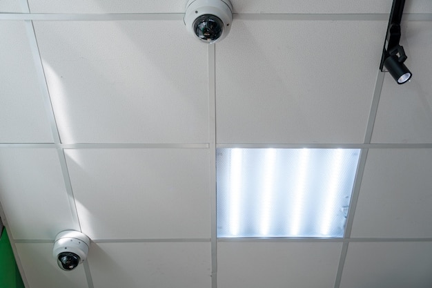 Caméras de surveillance modernes avec accès Internet à distance à l'intérieur du magasin Beau plafond de bureau avec lumières et lampes fluorescentes Caméras CCTV montées dans le plafond suspendu
