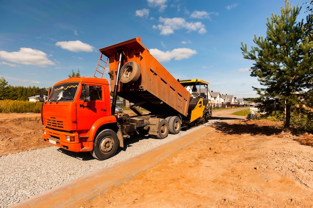 Un camion à benne décharge l'asphalte chaud dans un finisseur d'asphalte pour la construction d'une nouvelle route en été