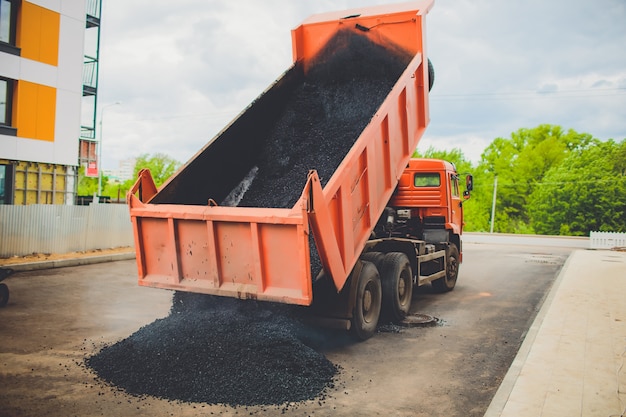 Un camion décharge de l'asphalte frais dans l'épandeur sur une grande route de la ville