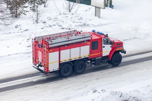 Un camion de pompier rouge roule sur une route enneigée.