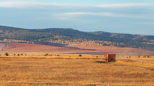 Un camion roule le long d'une route de campagne dans un champ avec une montagne en arrière-plan