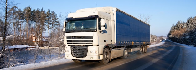 Le camion roule sur la route à travers la forêt d'hiver enneigée