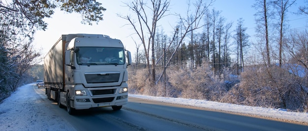 Le camion roule sur la route à travers la forêt d'hiver enneigée