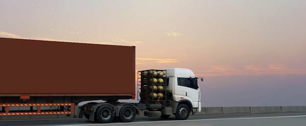 Camion sur route avec conteneur rouge, logistique industrielle avec ciel de lever du soleil