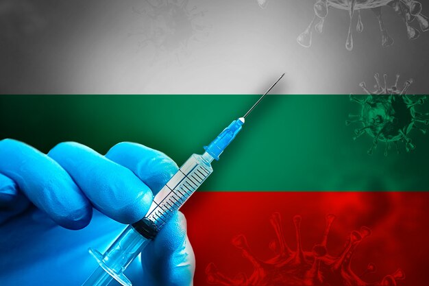 Campagne de vaccination de la Bulgarie Covid19 La main dans un gant en caoutchouc bleu tient une seringue devant le drapeau