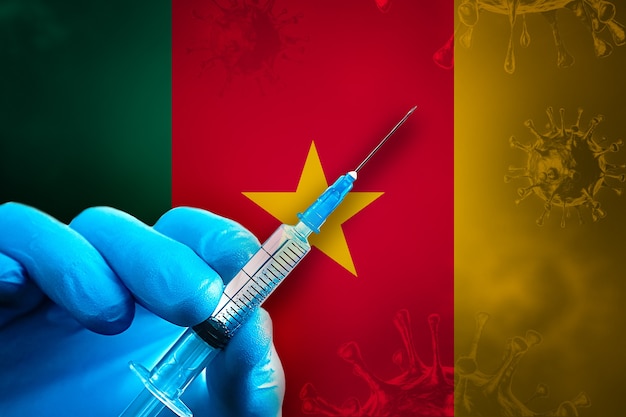 Campagne de vaccination contre le Covid19 au Cameroun La main dans un gant en caoutchouc bleu tient une seringue devant le drapeau