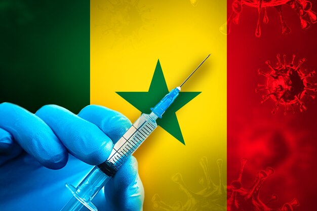 Campagne de vaccination du Sénégal Covid19 La main dans un gant en caoutchouc bleu tient une seringue devant le drapeau